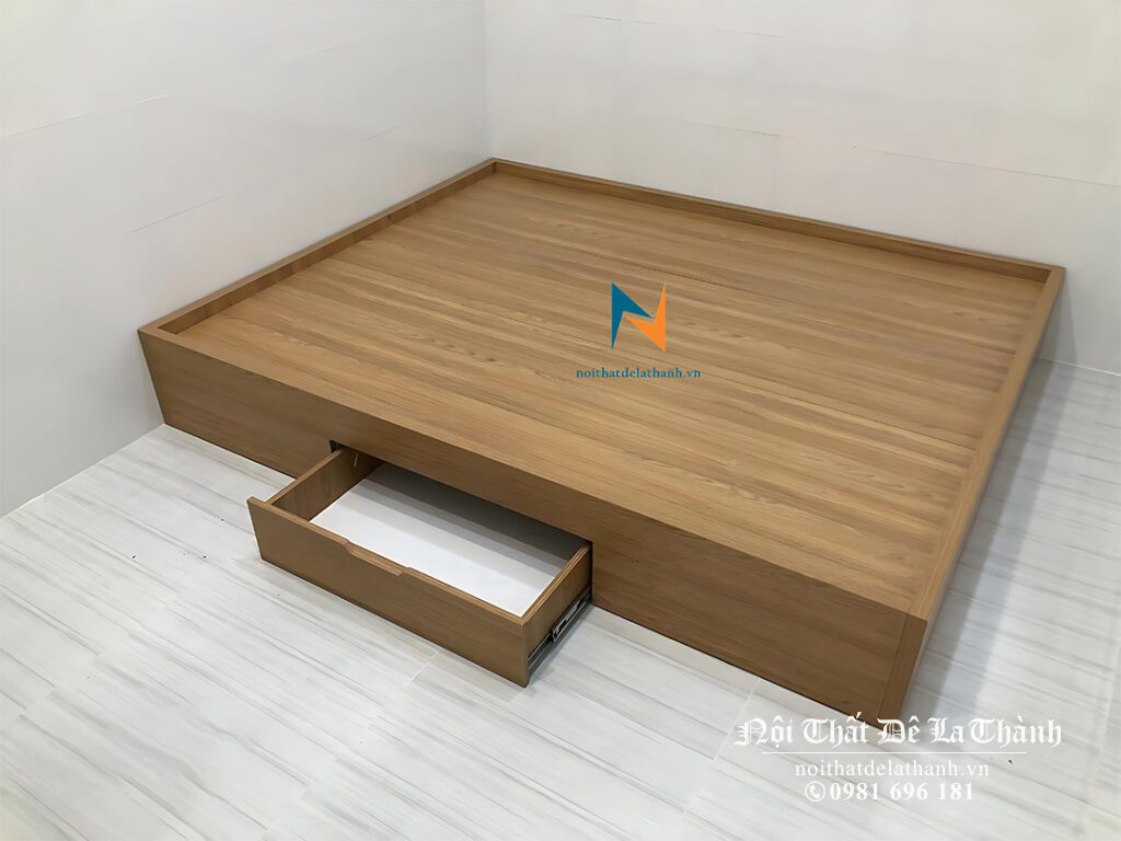 Chiếc giường bệt không đầu cao có ngăn kéo, kích thước 1m6x2m, màu nâu vân gỗ, vai trái có 1 ngăn kéo để đồ